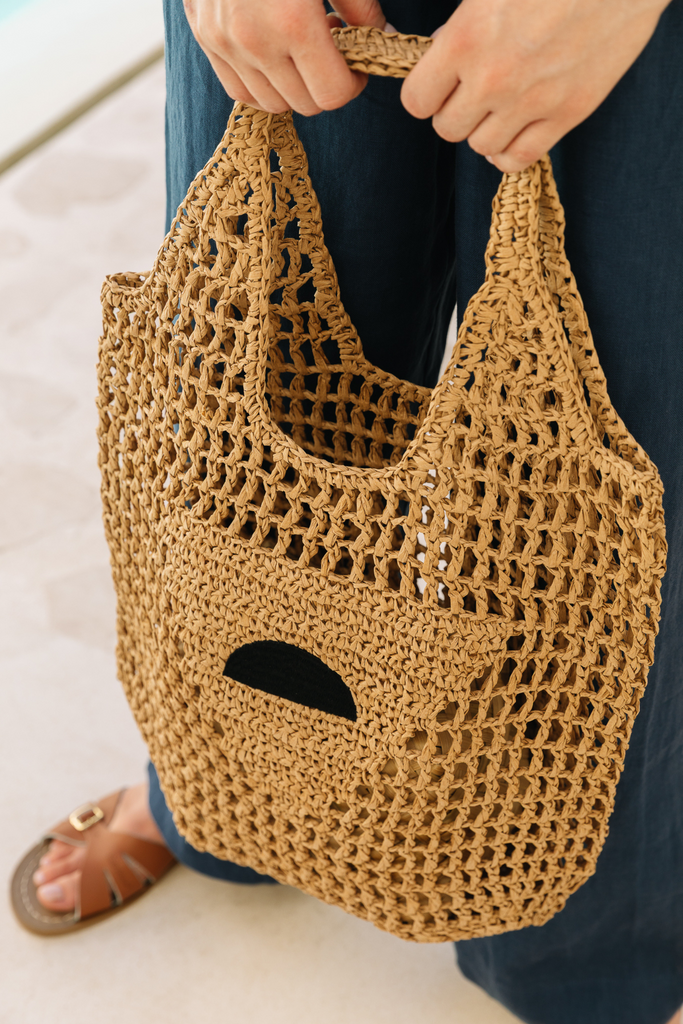 Model holding a raffia beach bag from Summery The Label, styled for a relaxed coastal day in the UK
