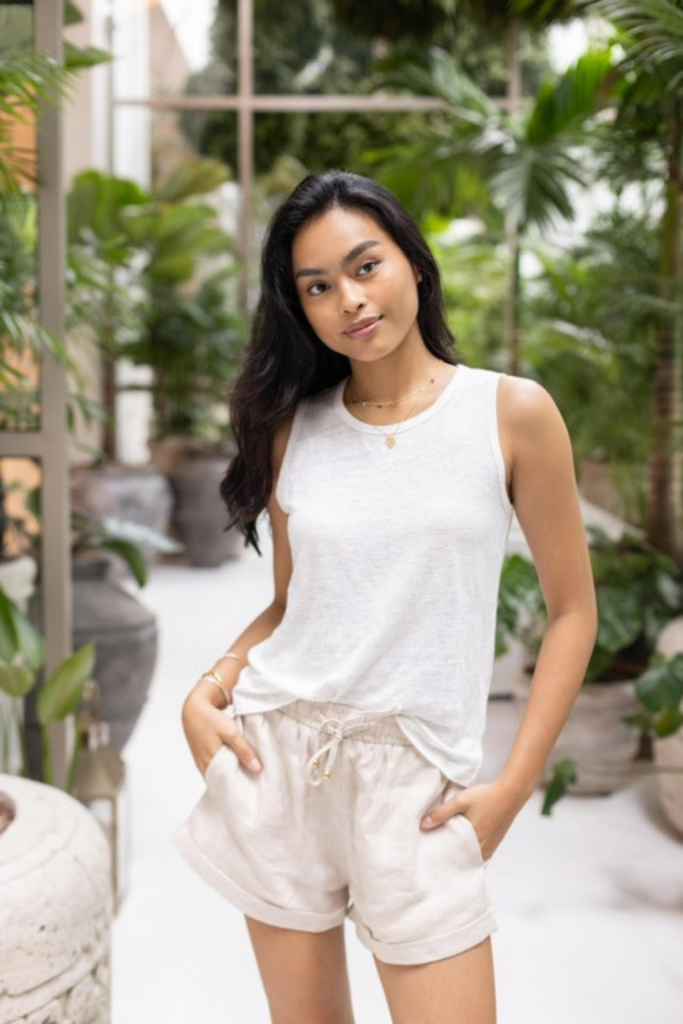 Model wearing Summery The Label’s linen shorts in oat, styled with matching linen sleeveless top in a tropical greenhouse setting.