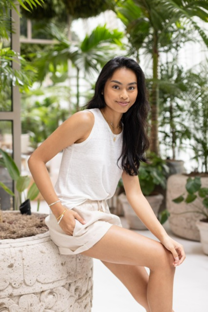 Model wearing Summery The Label’s linen shorts in oat, styled with matching linen sleeveless top in a tropical greenhouse setting.